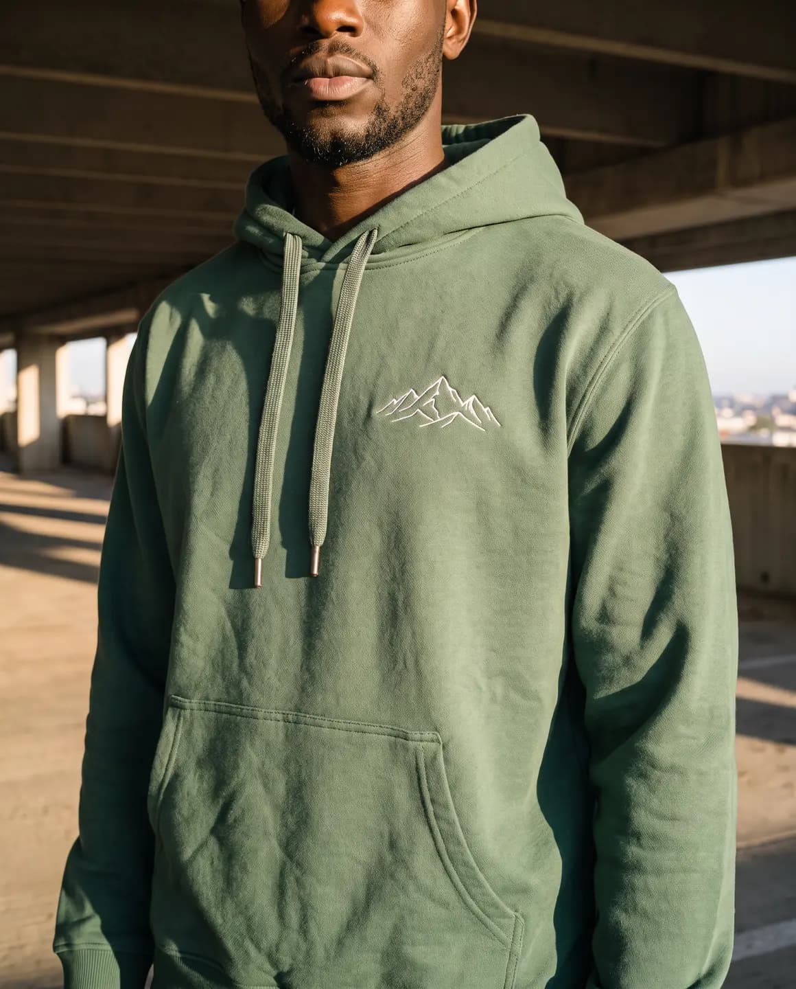 Green hoodie with drawstrings and a small white mountain emblem, close-up