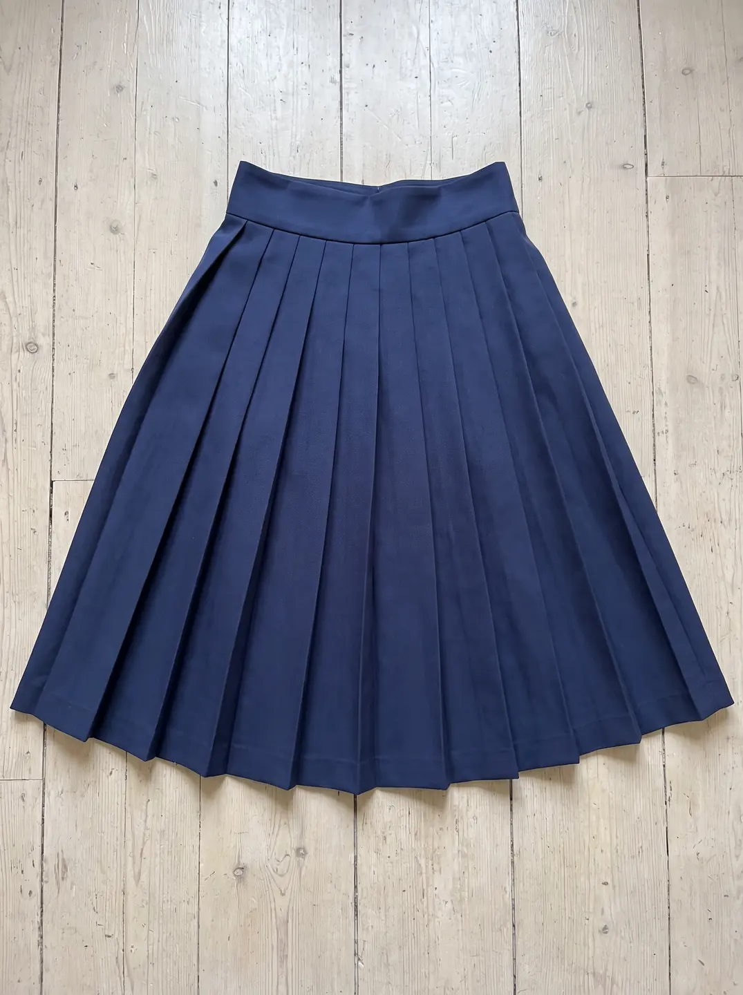 A navy pleated midi skirt laid flat on whitewashed floorboards
