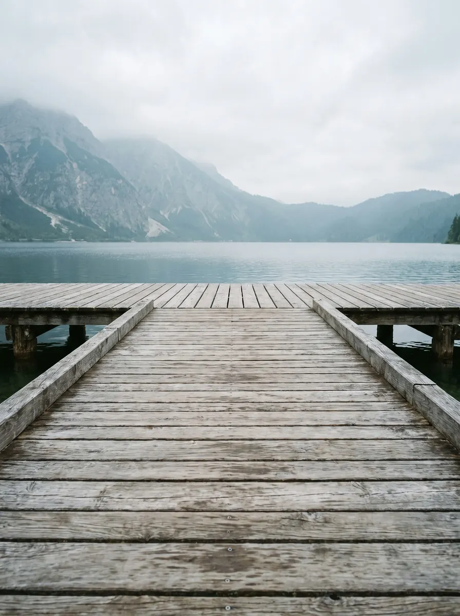 Weathered wooden dock reaching into a misty lake, with mountains in the background
