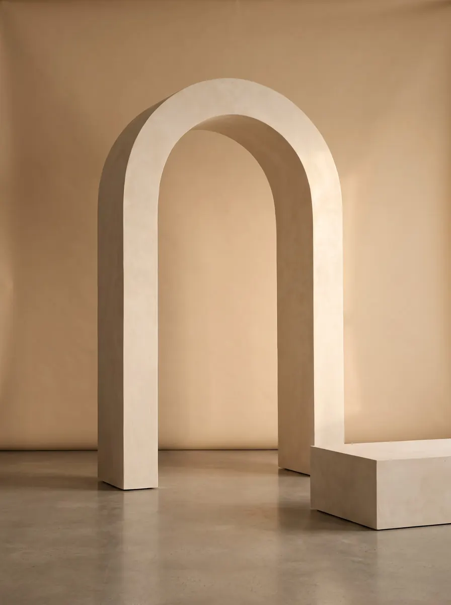 Limestone plaster arch and a low plinth on a concrete floor in a beige studio