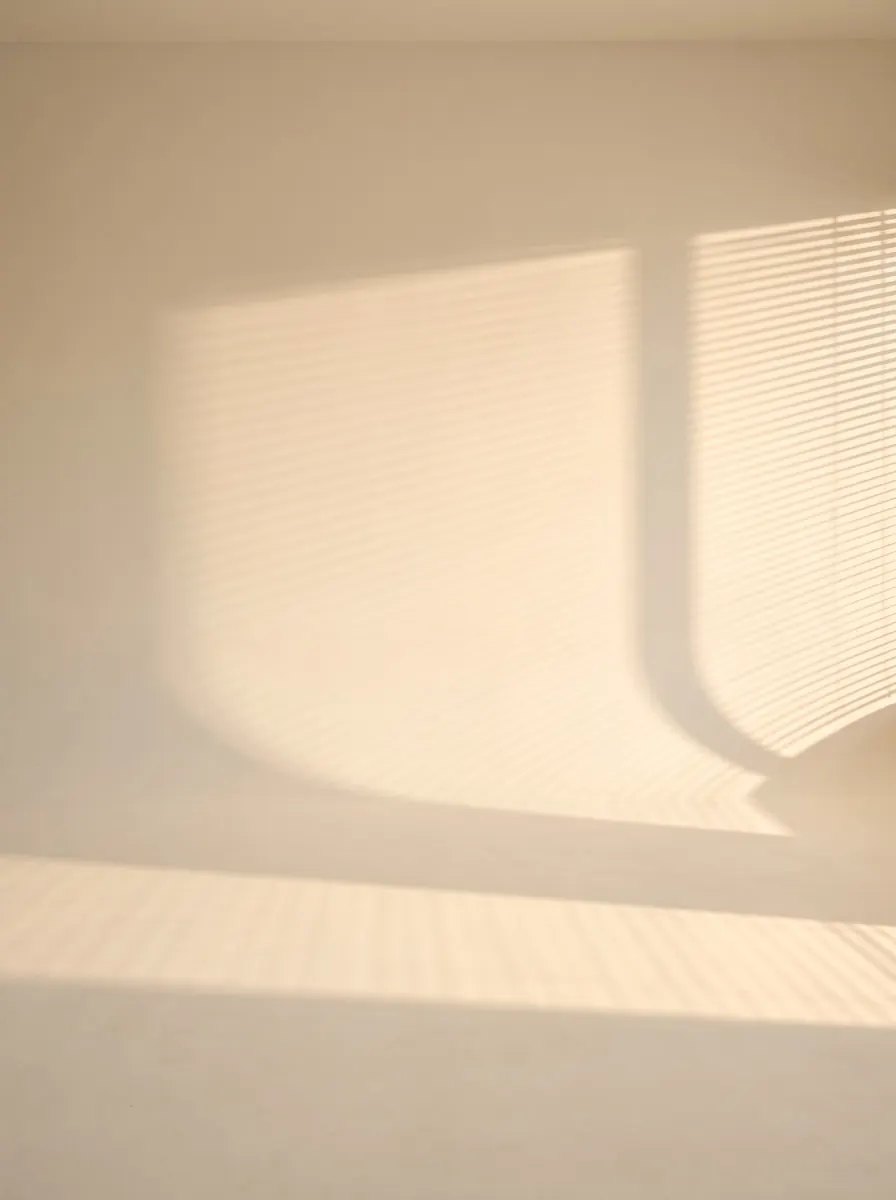 Warm cream wall and floor crossed by soft venetian-blind sun shadows